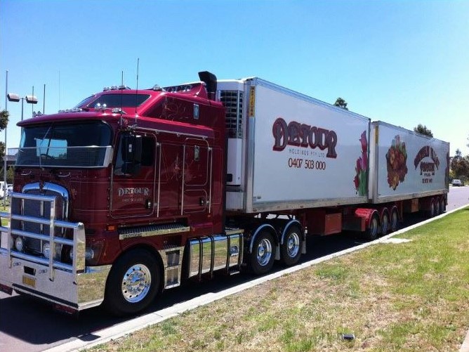 Red semi-truck with a long refrigerated double trailer parked roadside, featuring food product graphics and company branding on the trailer sides.