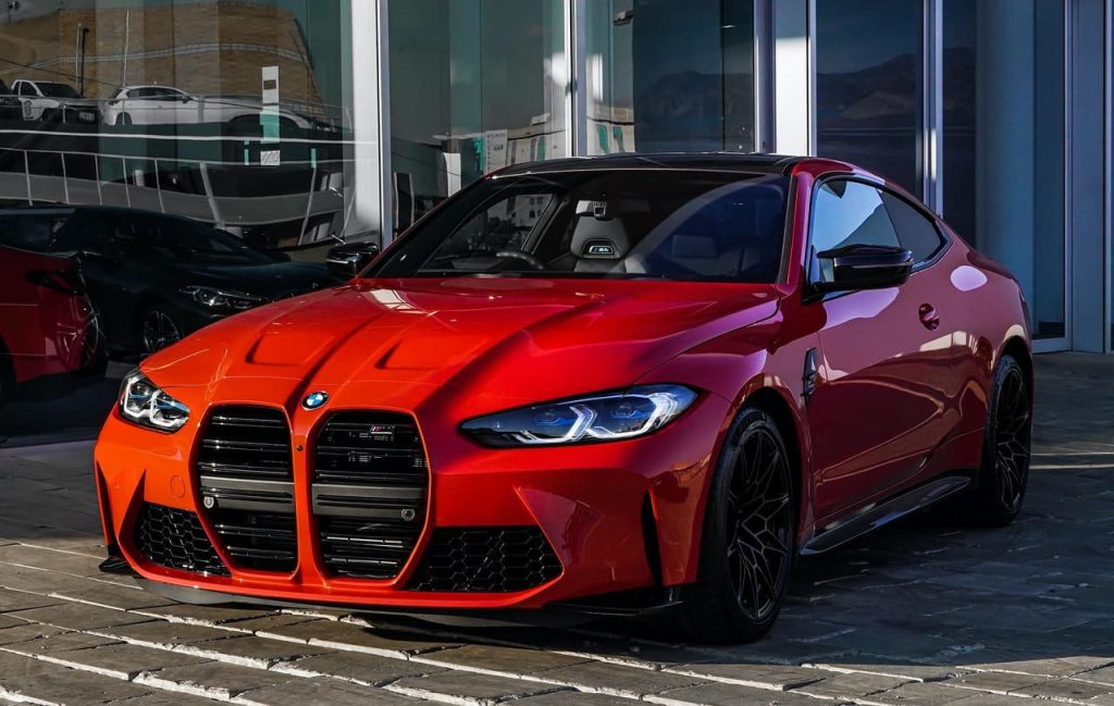 Red BMW sports coupe parked outside a modern glass-fronted building, featuring a low stance, black alloy wheels, and large front grille.